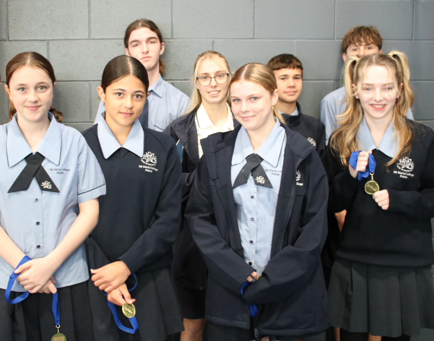 Group of students in school uniforms standing together, some holding medals.