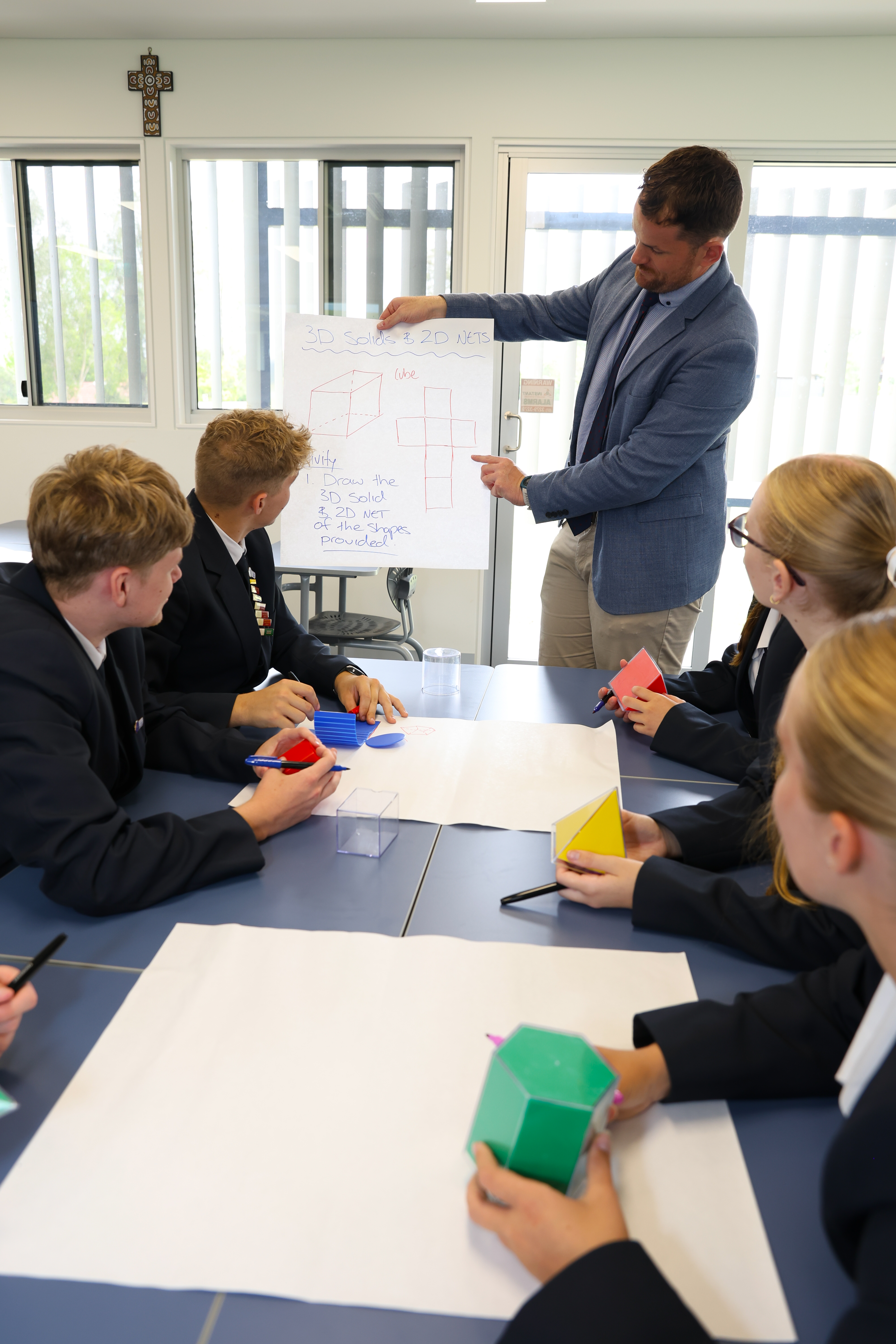 Group of students seated at a table while a teacher points to a chart at the front of the room